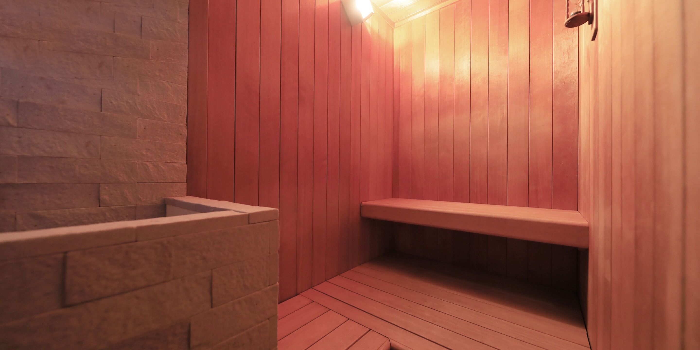 A sauna with wooden walls and benches, a stone bench, and a light fixture.