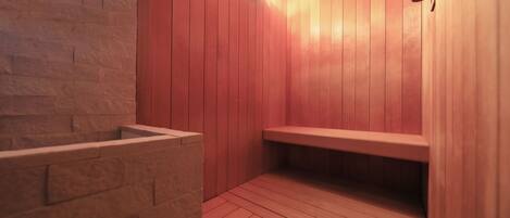 A sauna with wooden walls and benches, a stone bench, and a light fixture.