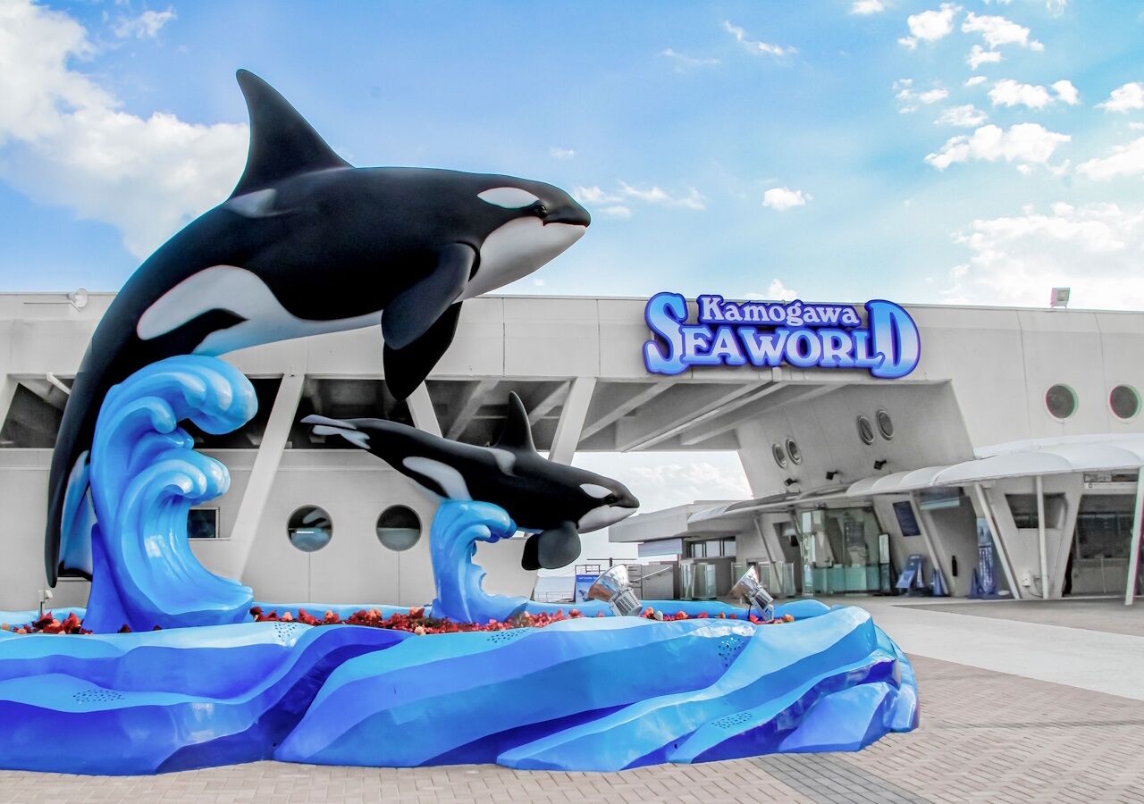 Una escultura de orca frente a un edificio con el letrero "Kamogawa SeaWorld".