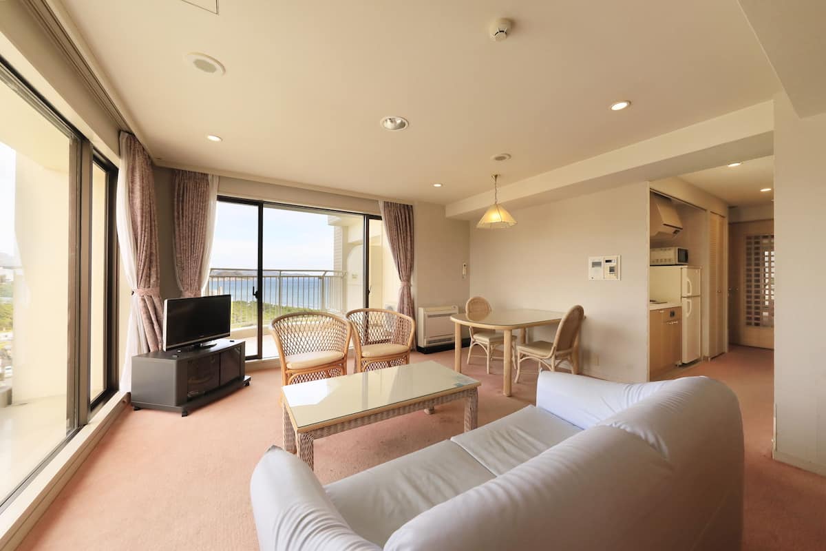 Une chambre d’hôtel moderne dotée d’une grande fenêtre, d’un téléviseur à écran plat, d’un canapé, d’une table à manger et d’une kitchenette.