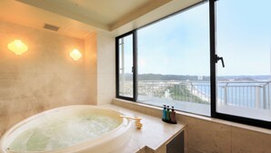 Un baño con una bañera, dos apliques, un ventanal con vista a un puente y un paisaje urbano, y un lavabo con dispensadores de jabón.