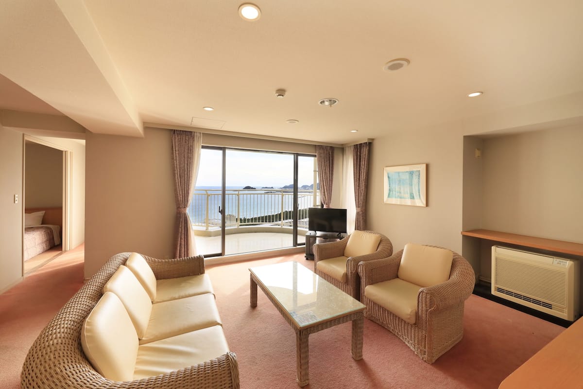 Une chambre d’hôtel avec balcon, des meubles en osier, un téléviseur à écran plat et une cheminée.