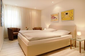 Habitación de hotel con una cama grande, dos sillones, una mesita y obras de arte en las paredes.