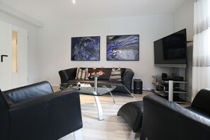 En moderne stue med en sort lædersofa, et glasbord og to abstrakte malerier på væggen.