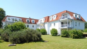 Un grand bâtiment blanc, doté d’un toit recouvert de tuiles rouges, de nombreux balcons et d’une pelouse bien entretenue.