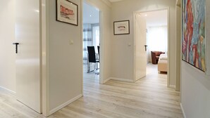 Un couloir d’hôtel avec un plancher en bois, des œuvres d’art encadrées accrochées aux murs et une vue sur un espace de restauration avec des chaises et une table.