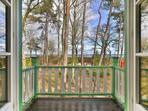 Eine Holzterrasse mit weißer Reling, mit Blick auf bewaldetes Gebiet.