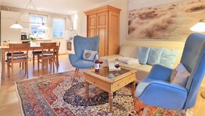 Un salon avec une table basse en bois, des fauteuils bleus, un canapé et un grand tableau abstrait accroché au mur.