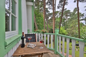 A wooden table with a bottle of wine and glasses on a balcony with a white railing, surrounded by greenery. - Landhaus Victoria, Seeschwalbe (Ostseebad Boltenhagen)