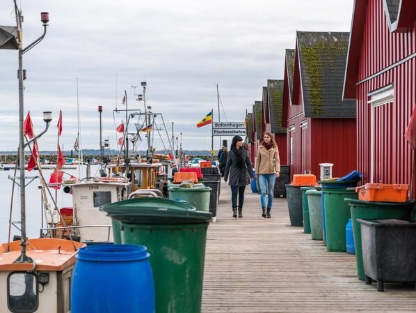 A wooden pier with boats and trash bins, leading to a red building with a sign.