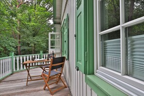 A wooden deck with a table and chairs, a white railing, and a window with green shutters.