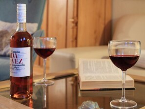 A bottle of wine, two wine glasses, and a book on a table.