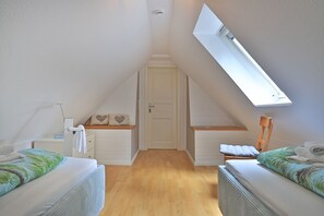 Una habitación pequeña y luminosa con techo inclinado, tragaluz y dos camas con cabeceros a juego.