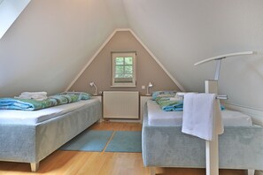 Un dormitorio ático pequeño y triangular con dos camas, una ventana y un radiador.