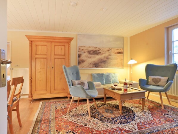 A living room with a wooden cabinet, two armchairs, a sofa, a coffee table, and a patterned rug.