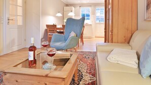 Un salon chaleureux avec un fauteuil bleu, une table basse en bois sur laquelle se trouvent une bouteille de vin et des verres, un canapé beige et un tapis à motifs.
