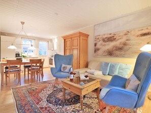 A living room with a wooden coffee table, blue armchairs, a sofa, and a large abstract painting on the wall. - Landhaus Victoria, Seeschwalbe (Ostseebad Boltenhagen)