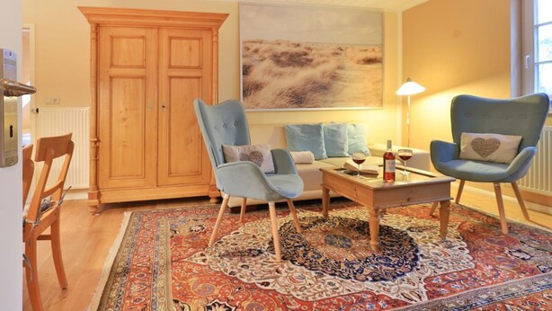 Un salon comprenant un meuble en bois, deux fauteuils, un canapé, une table basse et un tapis à motifs.