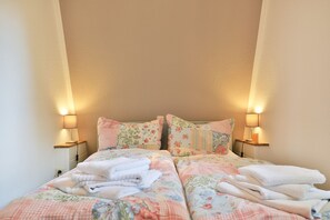 A double bed with floral bedding, two bedside lamps, and a stack of white towels.