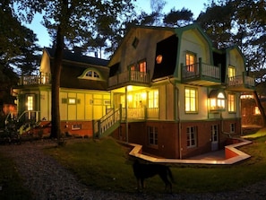 A large, multi-story house with a balcony, a staircase, and a well-lit front porch.