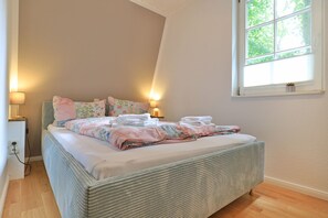 A cozy bedroom with a large bed, a bedside lamp, and a window with a view of greenery.
