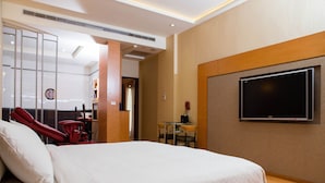 Hotelkamer met een bed, een televisie aan de muur, een bureau met stoel en een rode massagestoel.