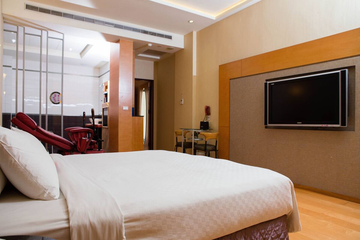 Ein Hotelzimmer mit Bett, einem an der Wand befestigten Fernseher, einem Schreibtisch mit Stuhl und einem roten Massagesessel.