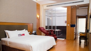 Hotelkamer met een groot bed, een rode relaxfauteuil, een klein tafeltje en uitzicht buiten door een glazen deur.