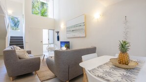 A modern living room with grey sofas, a dining table with a pineapple centerpiece, and a large beach-themed painting on the wall. - 69 Reef Resort | Poolside Private Villa (PORT DOUGLAS)