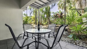A covered outdoor seating area with a table and chairs, a bottle of wine, and a pool entrance sign. - 69 Reef Resort | Poolside Private Villa (PORT DOUGLAS)