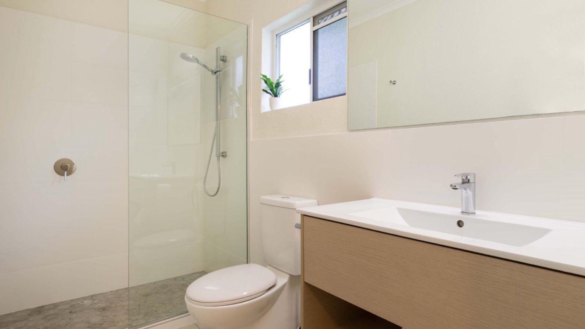Une salle de bain moderne avec une douche à parois de verre, des toilettes et un lavabo surmonté d’un miroir.