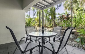 A covered outdoor seating area with a table and chairs, a bottle of wine, and a pool entrance sign.