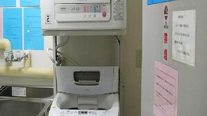 A kitchen with a built-in coffee machine, a sink, and a door with a bulletin board.