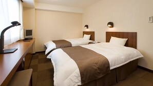 A hotel room with two beds, a desk with a lamp, a television, and a window with curtains.