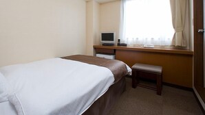 A hotel room with a bed, a desk with a computer, and a window with curtains.