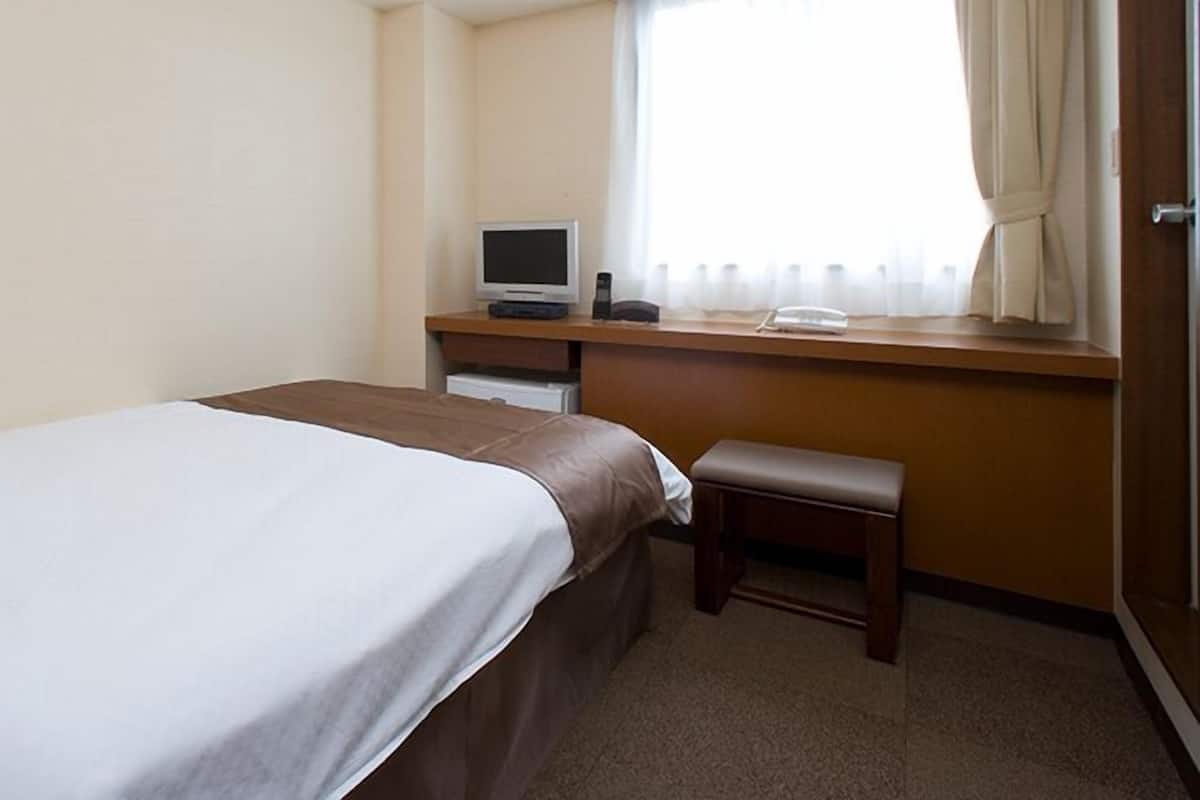 Een hotelkamer met een bed, een bureau met een computer en een raam met gordijnen.