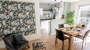 Une cuisine moderne avec un îlot central, un coin repas avec une table et des chaises en bois, et un espace de vie avec un canapé noir et un coussin vert.