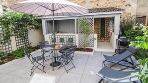 Une terrasse extérieure avec une table et des chaises, un grand parasol et un espace salon abrité.