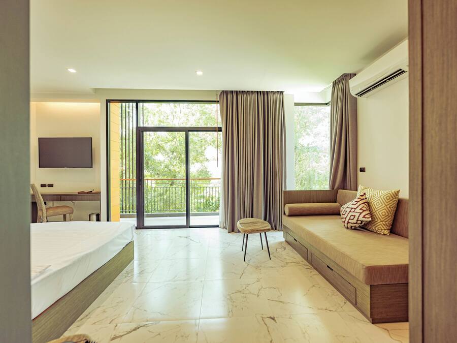 A modern hotel room with a bed, a sofa, a desk, and a large window with curtains.
