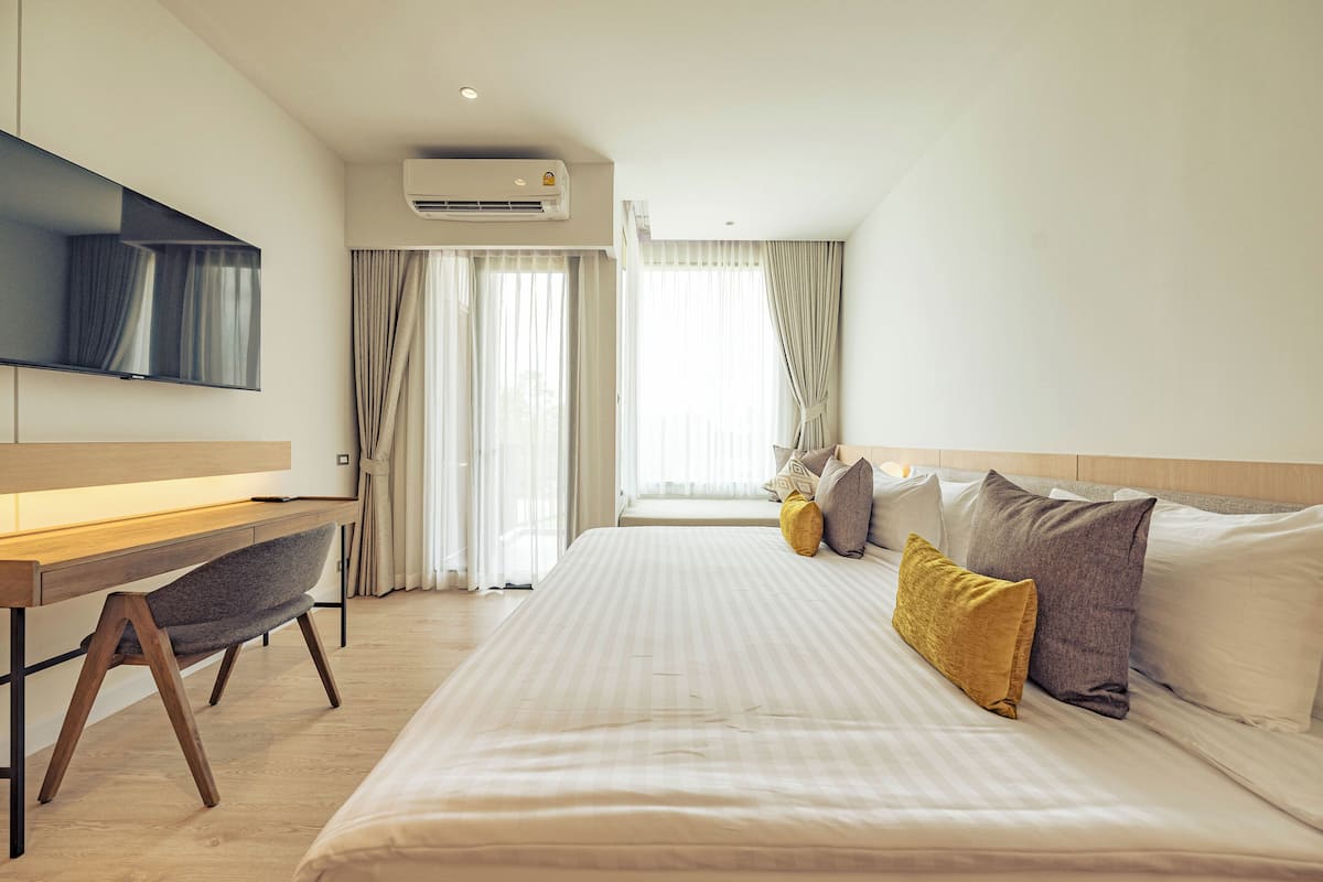 A hotel room with a bed, a desk, a chair, a television, and an air conditioning unit.