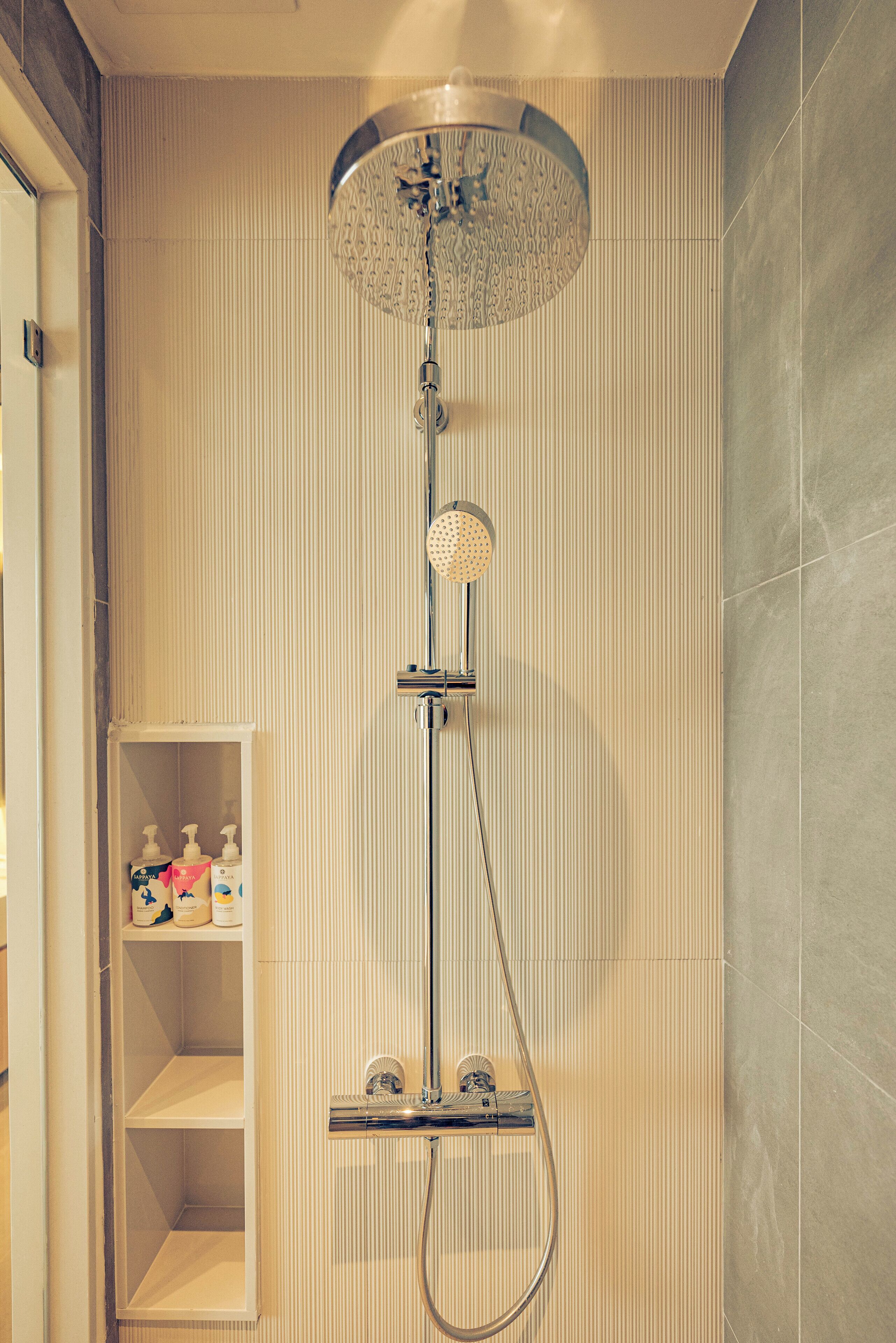 Eine moderne Dusche mit Regendusche und Handbrause, einem integrierten Ablagebereich für Pflegeprodukte und einer gefliesten Wand.