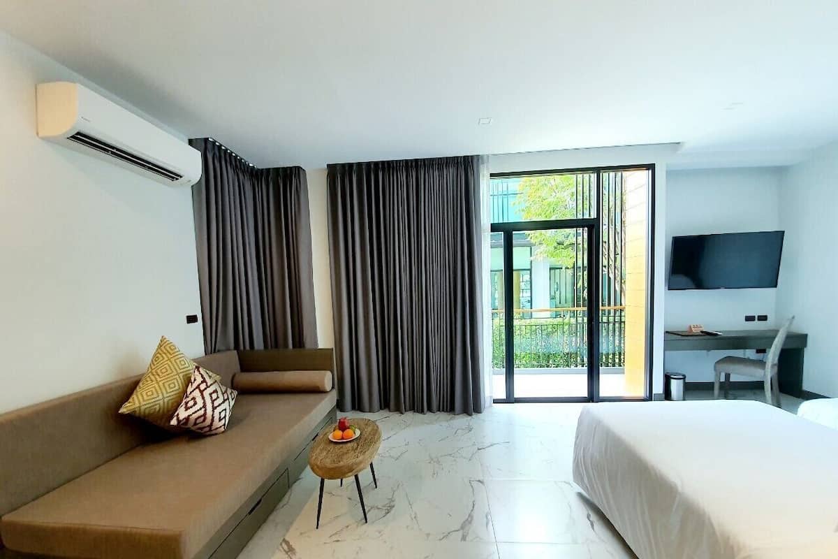 A hotel room with a sofa, a small round table with fruit, a bed, a desk with a chair, and a TV on the wall.