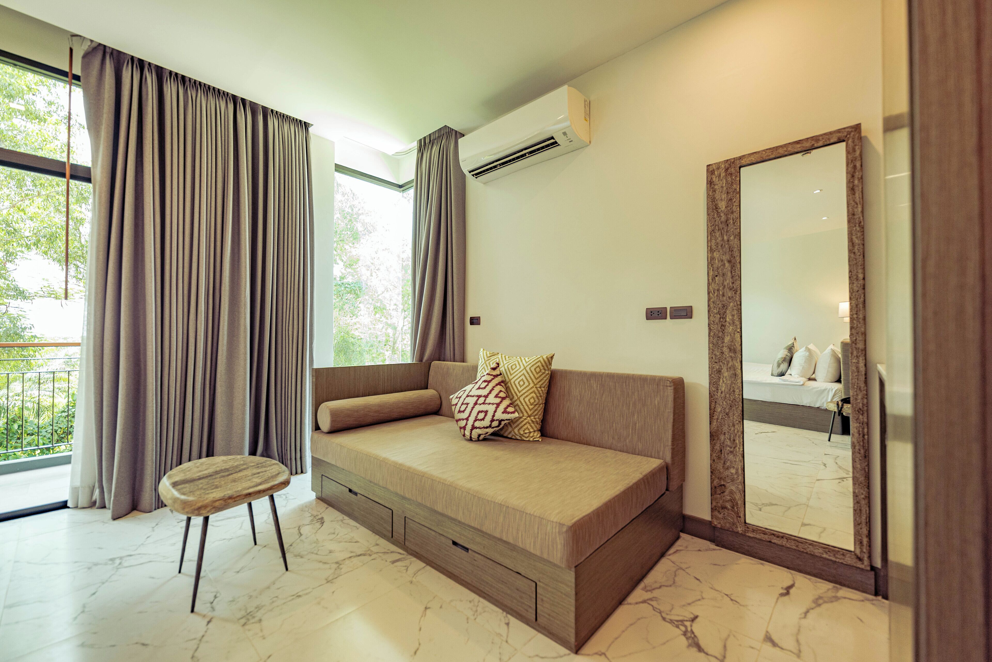 A modern room with a sofa, a small stool, a mirror, and an air conditioning unit.