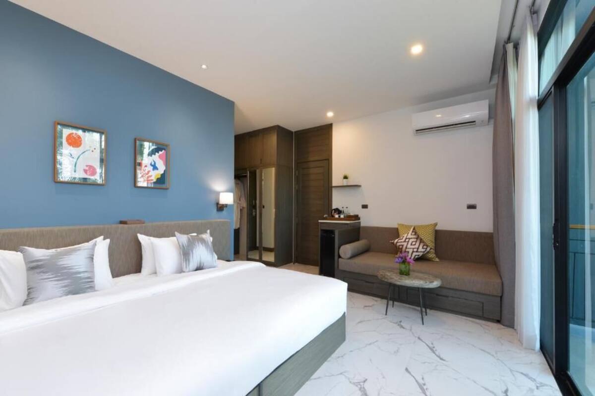 A modern hotel room with a large bed, a sofa, a small table, and artwork on the walls.