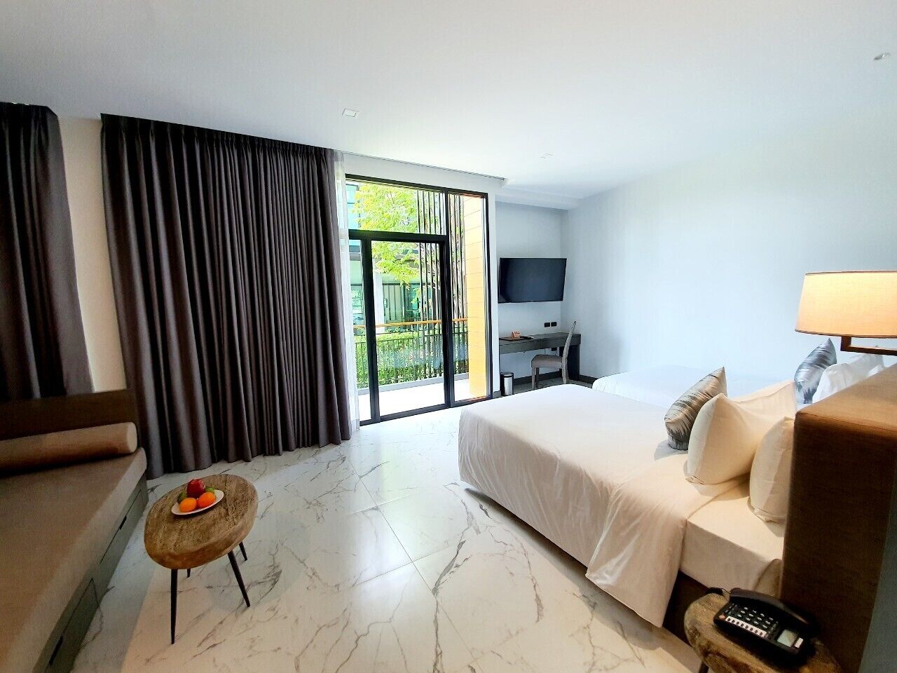 A hotel room with a bed, a desk, a TV, and a balcony with curtains.