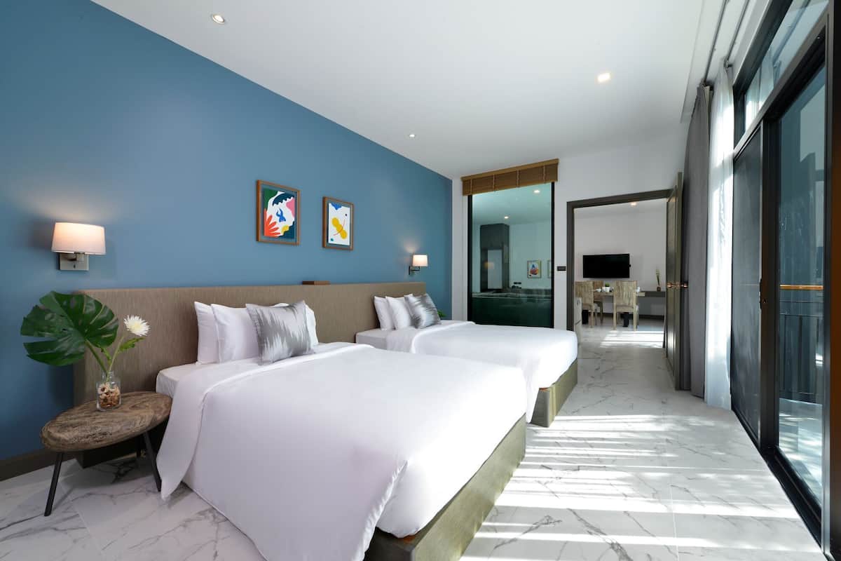 A hotel room with two beds, a large window, and a view of the hallway.