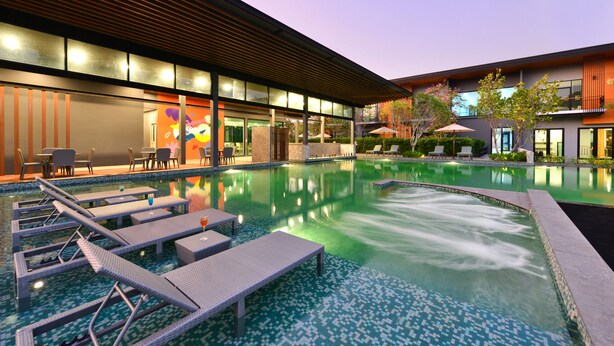 Un hotel moderno con piscina, sillones de descanso y zona de estar al aire libre.