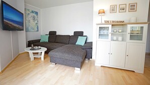 En stue med en grå hjørnesofa, et hvidt skab med glaslåger og et fladskærms-tv monteret på væggen.