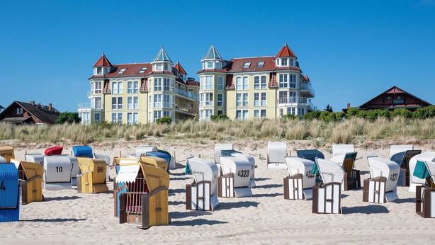En bygning ved stranden med flere balkoner og et sandstrand med nummererede strandhuse.