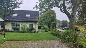 Uma casa com telhado inclinado, um pequeno jardim e uma entrada com calçada de brita.